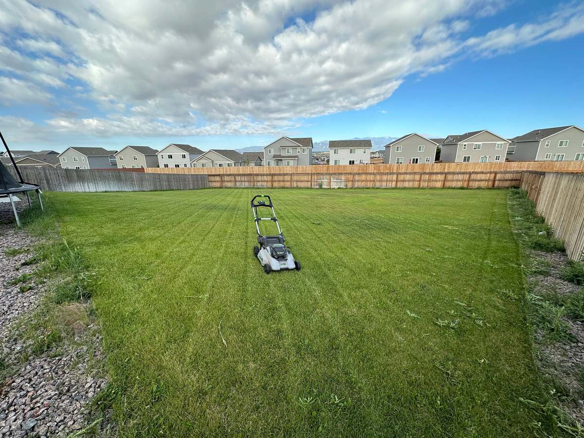 A Kaleo Lawncare battery powered mower parked mid-job on a large striped back lawn, with the Front Range visible beyond the fence