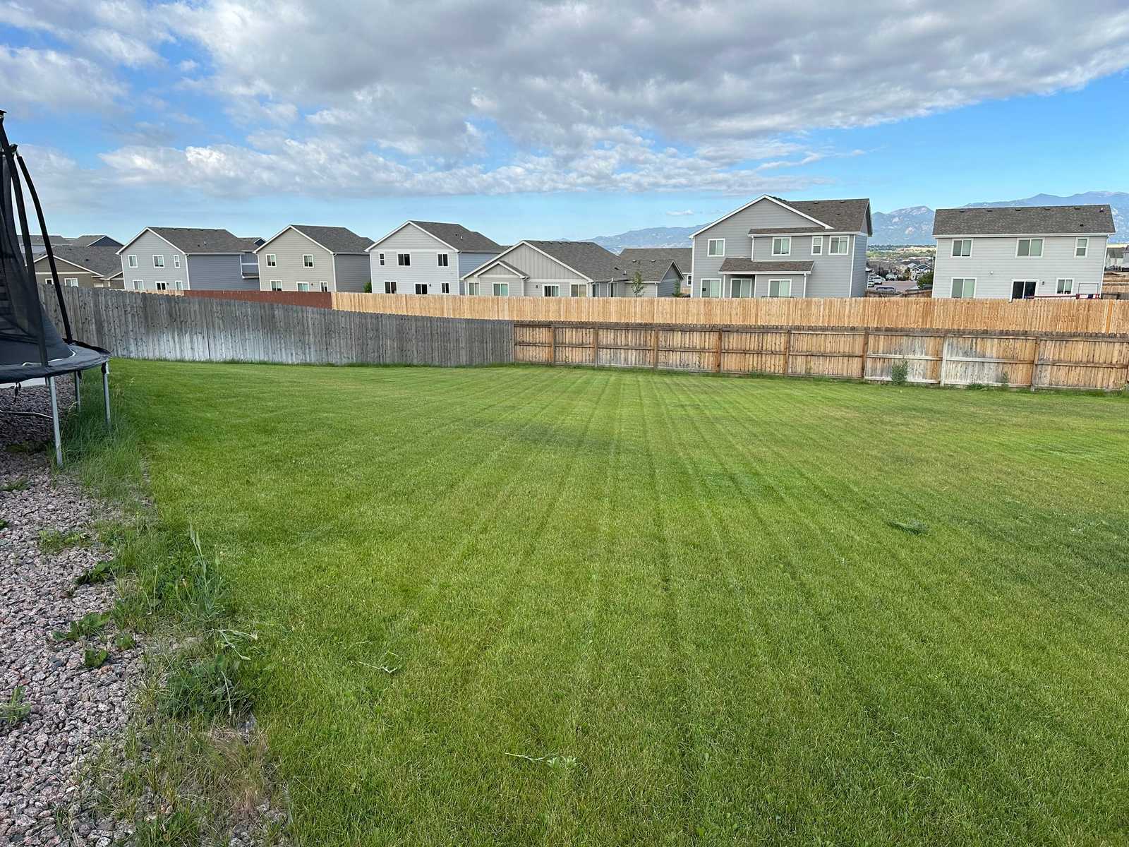 A wide back lawn in mown stripes, bounded by a timber fence with the Front Range beyond